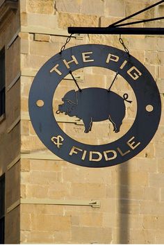 the pig and fiddle sign is hanging from a brick building with an arrow pointing to it