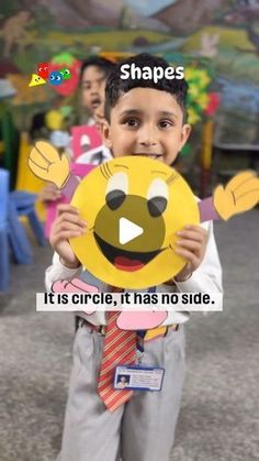 a young boy holding up a smiley face cutout with the words shapes it's circle, it has no side