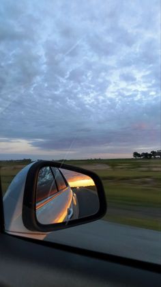 a car's side view mirror is shown as it drives down the road at dusk