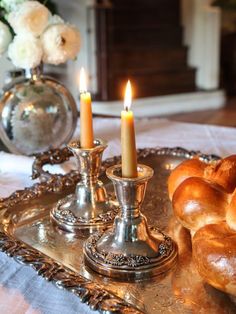 two candles are lit on a tray with breads and rolls in front of it