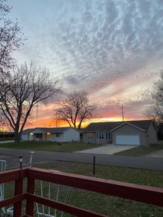 the sun is setting over some houses in an area that has grass and trees on both sides