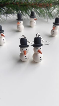 small snowmen wearing hats and scarves are hanging from silver earwires on a white surface