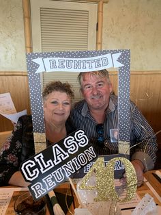 a man and woman sitting at a table in front of a sign that says class reunion