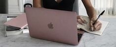 a woman sitting at a table with an apple laptop and notebook in front of her