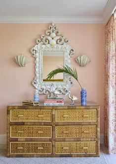 a dresser with a mirror and vase on top of it in front of a pink wall