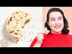 a woman holding a piece of food in front of her face and looking at the camera