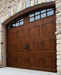 two brown garage doors in front of a brick wall and planter on the sidewalk