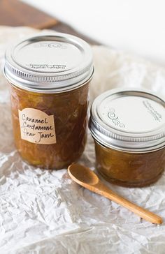 two jars of jam sitting on top of a table next to a spoon and wooden spoon