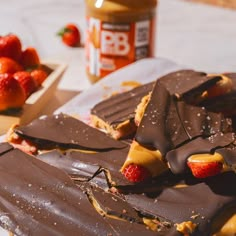 chocolate and strawberries are on the table next to some peanut butter bars with one bite taken out