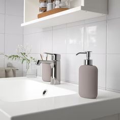 a bathroom sink with two soap dispensers on the shelf above it,