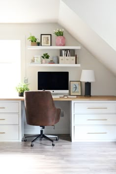 a desk with a computer on top of it in front of a white wall and some shelves