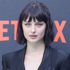 a close up of a person wearing a black suit and posing for the camera with an orange sign behind her