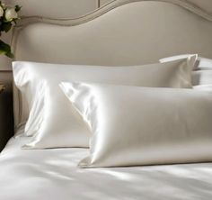 white sheets and pillows on a bed in a room with a vase full of flowers