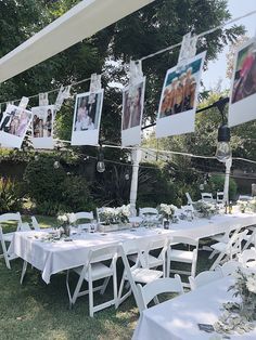 an outdoor wedding reception with white tables and pictures hanging from the line above them, surrounded by greenery