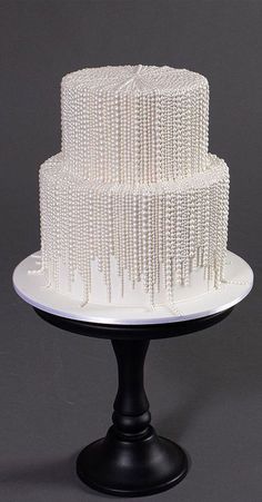 a three tiered white cake sitting on top of a black stand with beads all over it