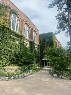 a large building covered in vines and flowers next to a sidewalk with trees on both sides