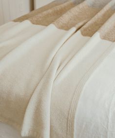 an unmade bed with white sheets and beige blankets