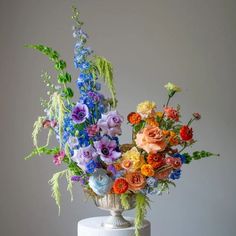 an arrangement of flowers is on top of a white cake with blue, orange and pink flowers