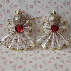 two christmas angel ornaments sitting on top of a white and gold cloth covered tablecloth