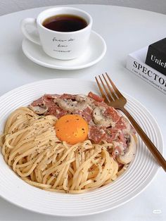 a white plate topped with pasta and an egg next to a cup of coffee on a table