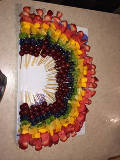 a platter with fruit and skewers arranged in the shape of a rainbow