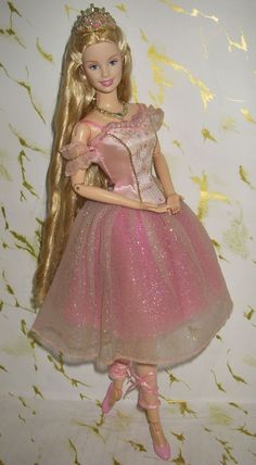 a barbie doll wearing a pink dress and tiara with long blonde hair standing in front of a white wall