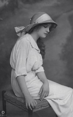 an old black and white photo of a woman in a hat sitting on a chair