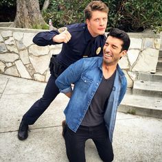 two men standing next to each other in front of some steps and trees with one man pointing at the camera