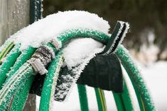 green hoses covered in snow next to a pole