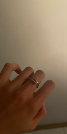 a person's hand with two wedding rings on their fingers in front of a white wall