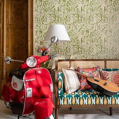 a red scooter is parked in front of a colorful couch and wallpaper