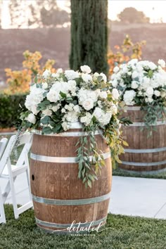 two wooden barrels with white flowers and greenery on the top are set up for an outdoor ceremony