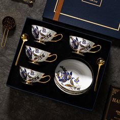 four cups and two saucers in a box with gold trimmings on them