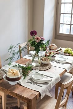 a wooden table topped with plates and bowls next to a vase filled with flowers on top of a hard wood floor