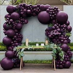 an arch made out of purple balloons and greenery with candles on the table in front