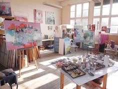 an artist's studio with easels and paintings on the table in front of large windows