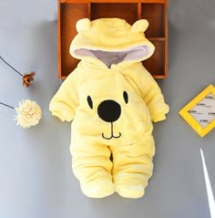 a yellow bear onesuit sitting on top of a table next to a flower vase