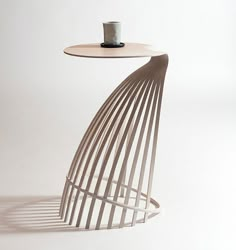 a white table with a cup on it and a wire sculpture next to it in the shape of a spiral