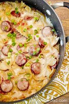 a skillet filled with pasta, sausage and cheese on top of a wooden table