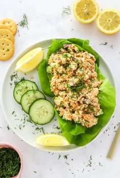 a white plate topped with lettuce covered in crab salad next to crackers and cucumbers