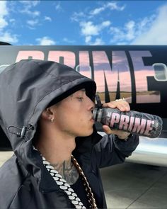 a man drinking from a can while standing in front of an airplane with the word prime written on it