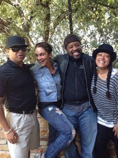 a group of people standing next to each other in front of a stone wall and tree