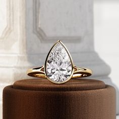 a gold ring with a pear shaped diamond on top of a brown velvet covered stand