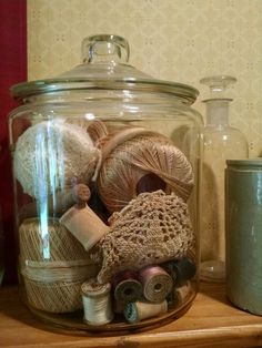 a glass jar filled with yarn and other items on a wooden shelf next to a canister