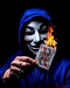 a person wearing a mask holding up a playing card with fire in front of them