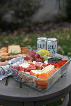 a glass bowl filled with fruit and crackers next to two cans of sodas