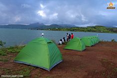 there are many tents set up by the water with people standing around them on the shore