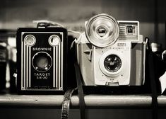 two old cameras sitting next to each other on a shelf