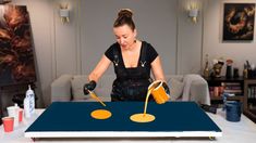 a woman pouring liquid onto a table with two yellow circles on it and another person in the background