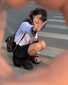 a woman kneeling down on the ground making a hand gesture